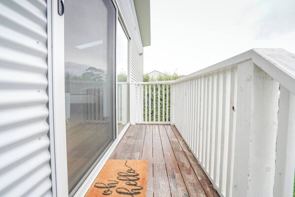 Una terraza de madera con barandilla blanca, puerta corrediza de vidrio y felpudo con la palabra 'hello'.