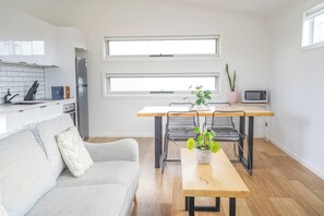 Una cocina moderna con armarios blancos, una mesa de comedor de madera y dos sillas. Hay una planta sobre la mesa y un microondas en la encimera.
