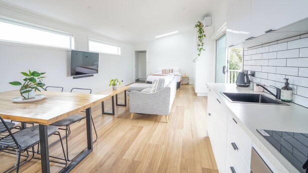 A modern kitchen with a dining area, a flat-screen TV mounted on the wall, and a small plant on the table.