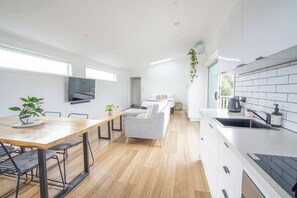 A modern kitchen with a dining area, a flat-screen TV mounted on the wall, and a small plant on the table. - Charming Highton Hideaway between CBD and Surf Coast (Highton)