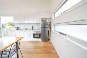 A modern kitchen with white cabinets, a stainless steel refrigerator, and a built-in oven. - Charming Highton Hideaway between CBD and Surf Coast (Highton)