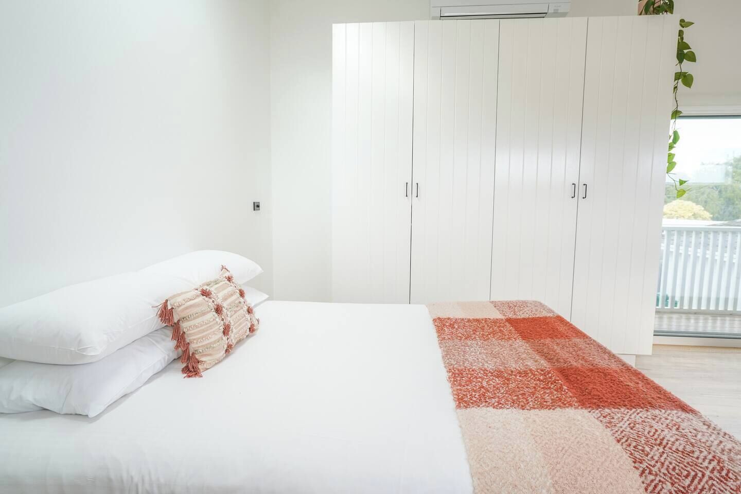 A bedroom with a bed, white walls, a white wardrobe, and a window with a view.