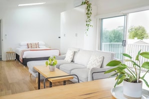 Una habitación moderna y bien iluminada con una cama, un sofá, una mesa de comedor y una planta en maceta.