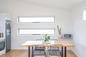 Una cocina moderna con una mesa de madera, dos sillas, un refrigerador, un horno, un microondas y dos ventanas.