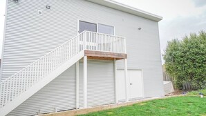A two-story building with a white exterior, a wooden staircase leading to a balcony, and a garage door.