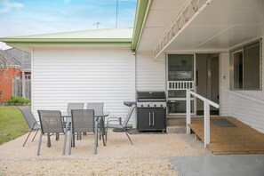 Eine Terrasse mit Grill, Sitzgelegenheiten im Freien und einem überdachten Bereich mit Treppe.