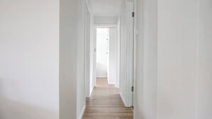 A narrow hallway with white walls and wooden flooring leading to a bright room. - Breezy Beach Shack Footsteps to Sand and Surf (Ocean Grove)