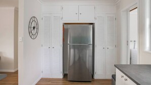 A kitchen with white cabinets, a stainless steel refrigerator, and a clock on the wall. - Breezy Beach Shack Footsteps to Sand and Surf (Ocean Grove)