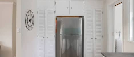 Une cuisine avec des armoires blanches, un réfrigérateur en acier inoxydable et une horloge au mur.