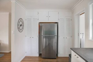 Eine Küche mit weißen Schränken, einem Edelstahlkühlschrank und einer Wanduhr.