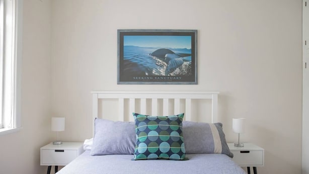 A bedroom with a bed, two bedside tables, a framed picture on the wall, and a window. - Breezy Beach Shack Footsteps to Sand and Surf (Ocean Grove)