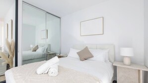 A hotel room with a bed, a bedside table with a lamp, a mirror, and a large window. - Perched on Parkville A Minimalist Retreat w Pool (Parkville)