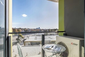 A balcony with a view of a cityscape, a Mitsubishi Electric air conditioning unit, and a table with a newspaper. - Perched on Parkville A Minimalist Retreat w Pool (Parkville)