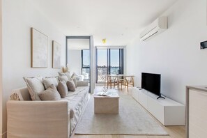 A modern living room with a sofa, TV, and a dining area with chairs. - Perched on Parkville A Minimalist Retreat w Pool (Parkville)