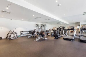 Une salle de sport équipée de divers appareils d’exercice, notamment des tapis de course, des appareils de musculation et des poids libres.
