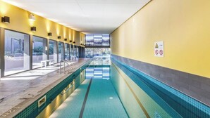 An indoor swimming pool with clear glass walls, a yellow wall on one side, and a tiled floor. - Perched on Parkville A Minimalist Retreat w Pool (Parkville)