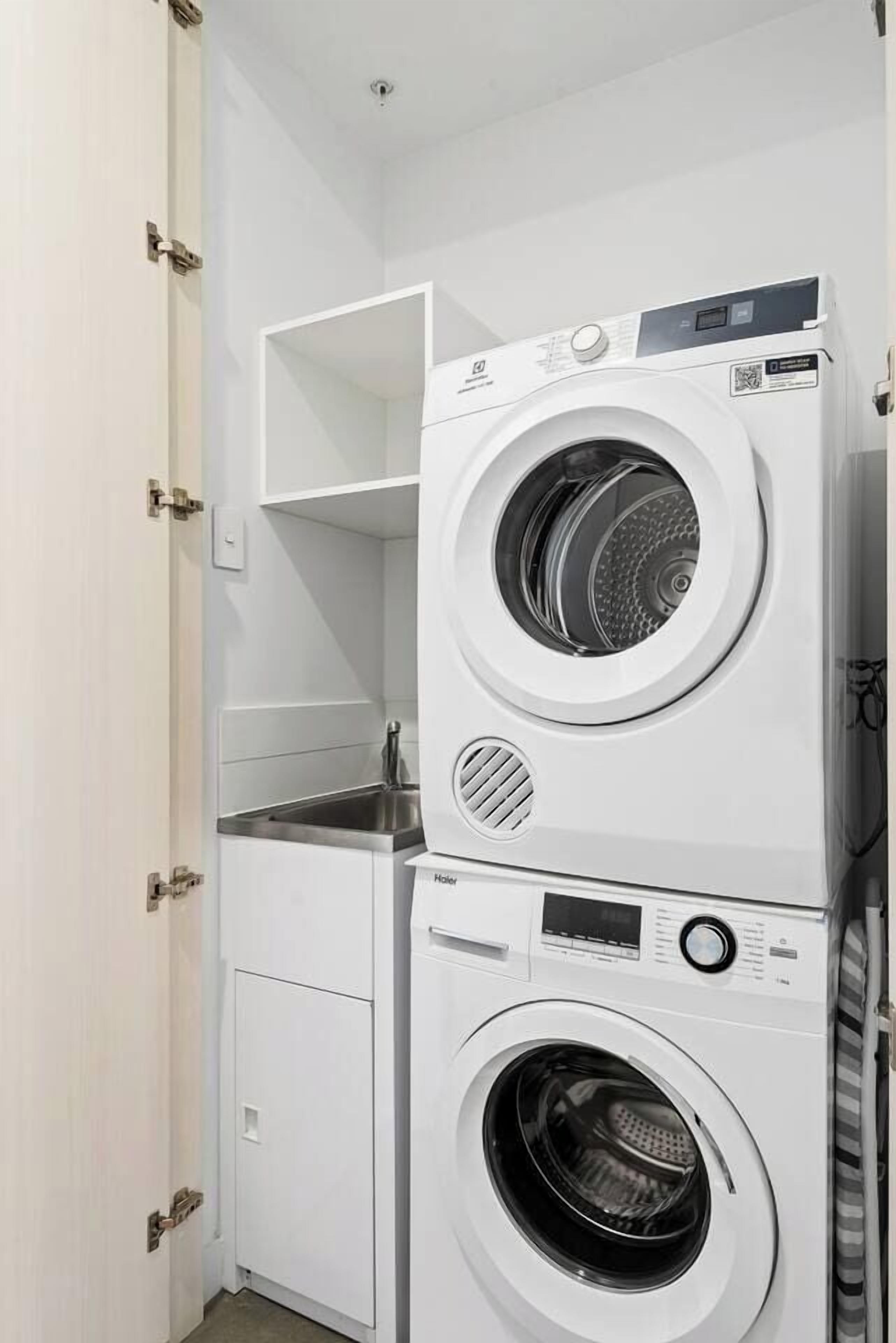 Een functionele wasruimte met een gestapelde wasmachine en droger, een klein wasbakje en een kastje.