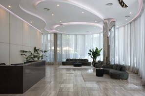 A modern reception area with a curved ceiling, a reception desk, a seating area with sofas, and large windows with sheer curtains. - Panoramic Elegance Stylish off Chapel St with Pool (South Yarra)