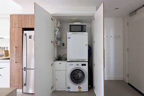 A compact kitchen with a built-in washer and dryer, a microwave, and a refrigerator. - Panoramic Elegance Stylish off Chapel St with Pool (South Yarra)