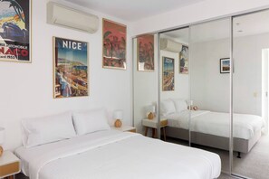 A hotel room with a large bed, a bedside table with a lamp, a small table with a vase, and a large mirror. - Panoramic Elegance Stylish off Chapel St with Pool (South Yarra)