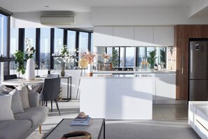 A modern kitchen with a central island, large windows, and a dining area with a sofa and coffee table. - Panoramic Elegance Stylish off Chapel St with Pool (South Yarra)