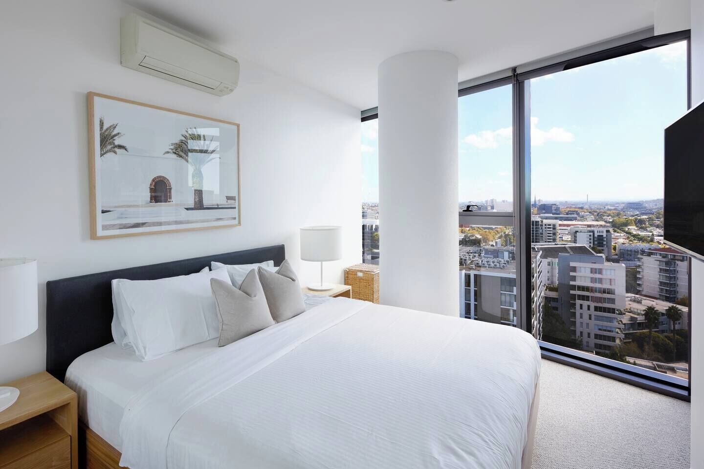 Ein modernes Hotelzimmer mit einem großen Bett, Blick auf die Stadt und einem gerahmten Kunstwerk an der Wand.