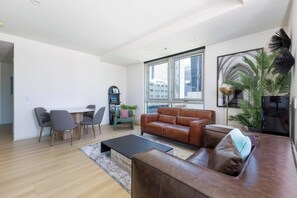Ein modernes Wohnzimmer mit einem braunen Ledersofa, einem Esstisch mit Stühlen, einem Couchtisch und einem großen Fenster mit Blick auf die Stadt.