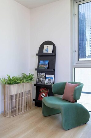 A room with a green armchair, a black bookshelf with magazines, and a plant in a wooden basket. - Citylight Haven Urban Comfort near Melbourne Icons (West Melbourne)