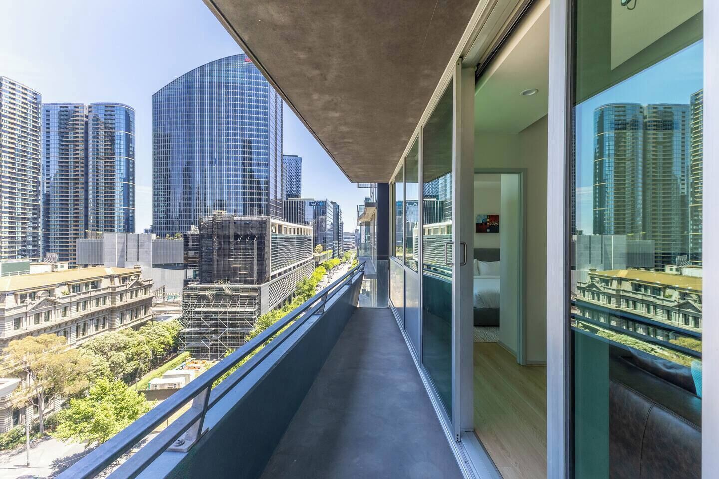 A modern balcony with a city view, glass railings, and a contemporary interior.