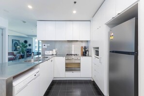 A modern kitchen with white cabinets, stainless steel appliances, and a black tiled floor. - Citylight Haven Urban Comfort near Melbourne Icons (West Melbourne)