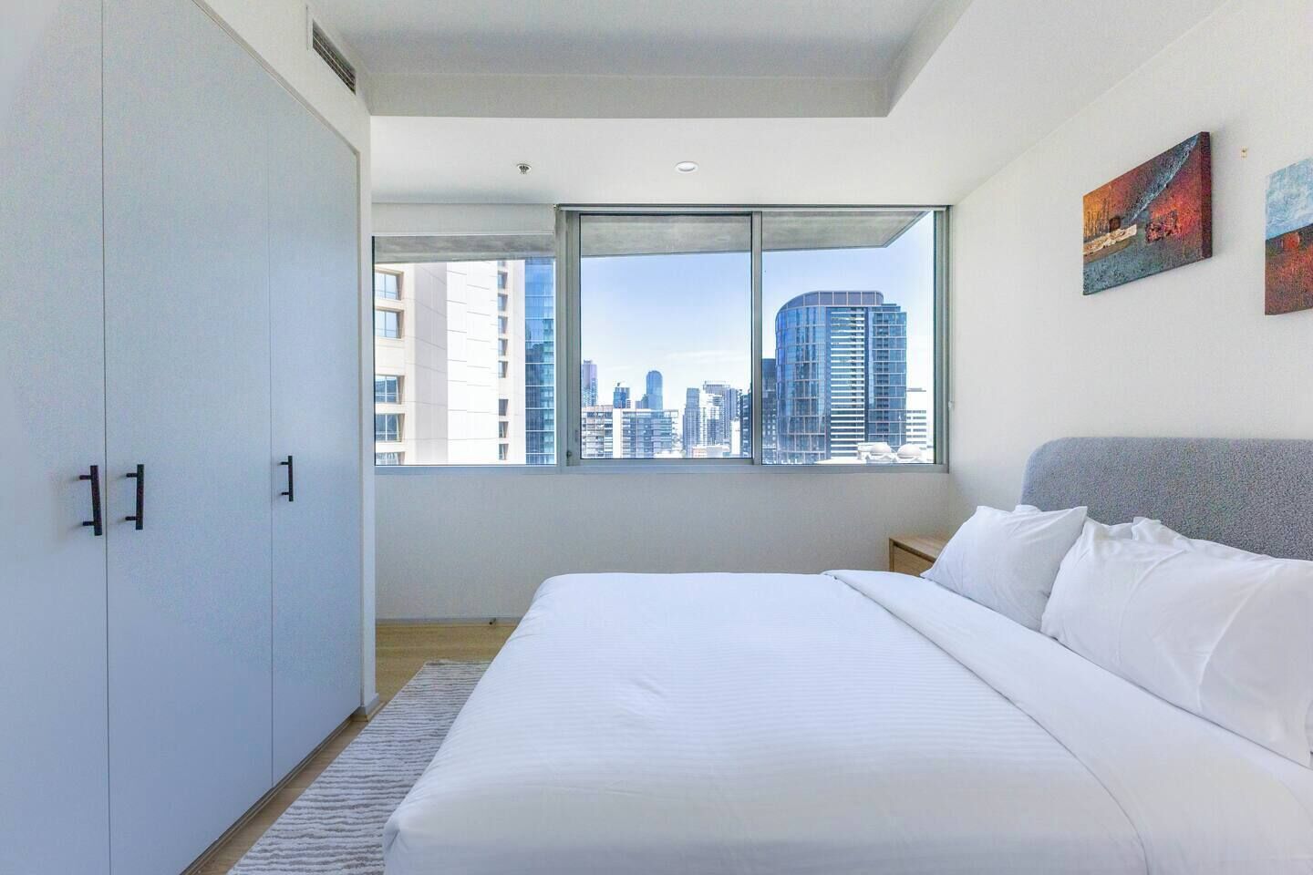 A modern bedroom with a large bed, a wardrobe, and a city view through a window.