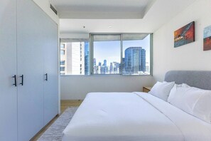Ein modernes Schlafzimmer mit einem großen Bett, einem Kleiderschrank und Blick über die Stadt durch ein Fenster.