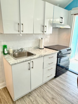 A kitchen with white cabinets, a stainless steel sink, a black oven, and a marble countertop.