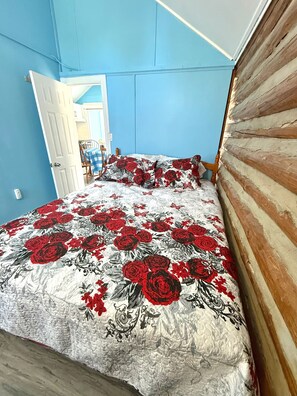 A room with a bed featuring a floral bedspread, a wooden headboard, and a door leading to another room.