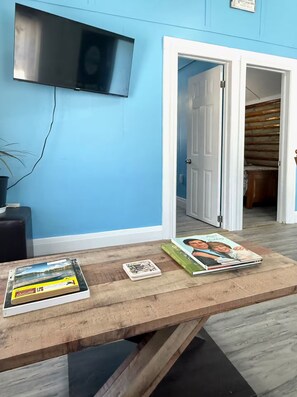 A room with a wooden table displaying books and a television mounted on the wall.