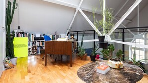 A spacious room with a high ceiling, a wooden desk, a round marble table, and various potted plants. - Hoffman Square - Two Bedroom Apartment, Sleeps 4 (London)