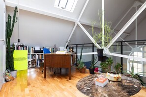 A spacious room with a high ceiling, a wooden desk, a round marble table, and various potted plants. - Hoffman Square - Two Bedroom Apartment, Sleeps 4 (London)