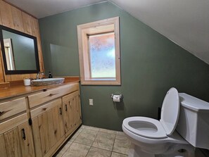 Een badkamer met een houten wastafelmeubel, een wit toilet en een raam met gezandstraald glas.