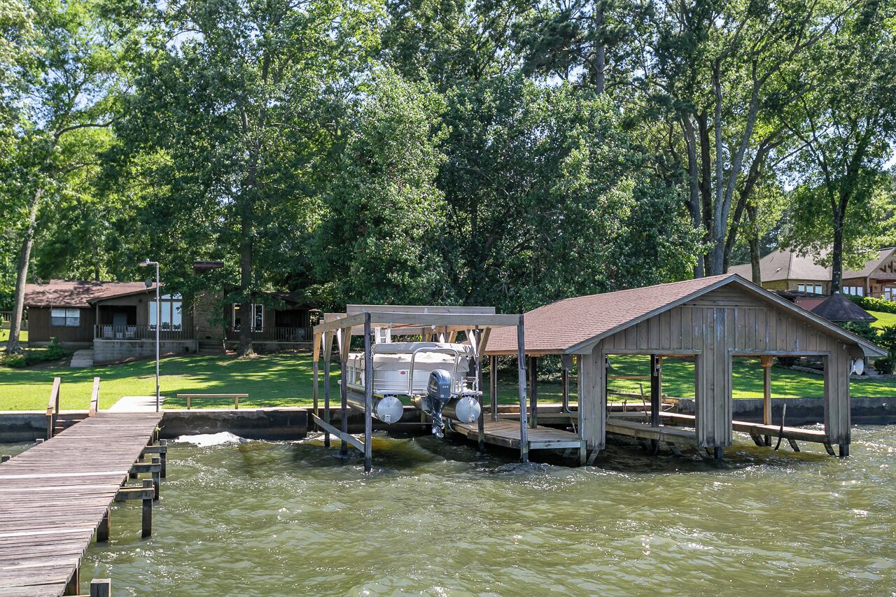 Un quai avec un bateau, une structure en bois et une zone herbeuse avec des arbres.