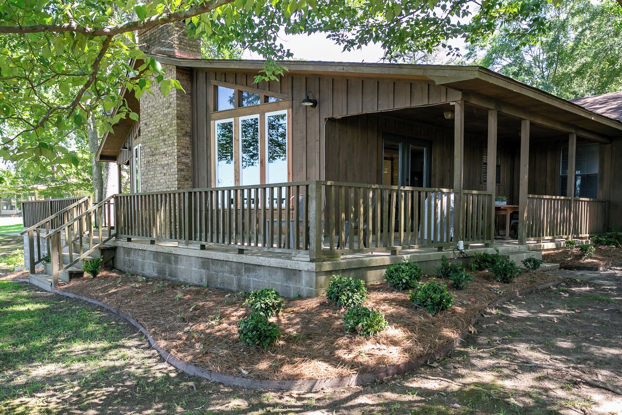 A wooden cabin with a porch, stone foundation, and a small garden area.