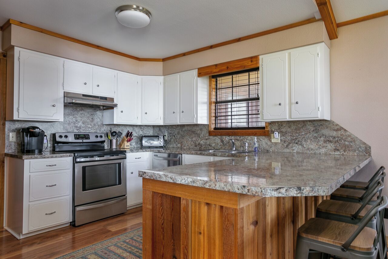 A kitchen with white cabinets, a granite countertop, stainless steel appliances, and a window with blinds.