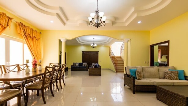 A spacious living area with a dining table, sofas, and a staircase leading to another level.