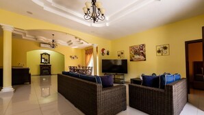 A living room with a large flat-screen TV, wicker sofas, and a chandelier.