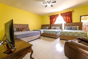 A hotel room with two beds, a television, a ceiling fan, and a brown leather chair.
