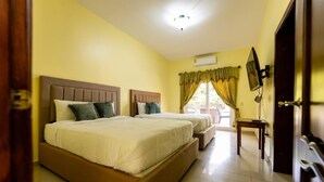 A hotel room with two beds, a television, and a window with curtains.