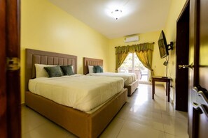 A hotel room with two beds, a television, and a window with curtains.