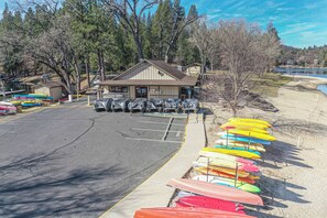 A parking lot with a row of canoes and kayaks on the right, a building with a brown roof in the center, and trees in the background.