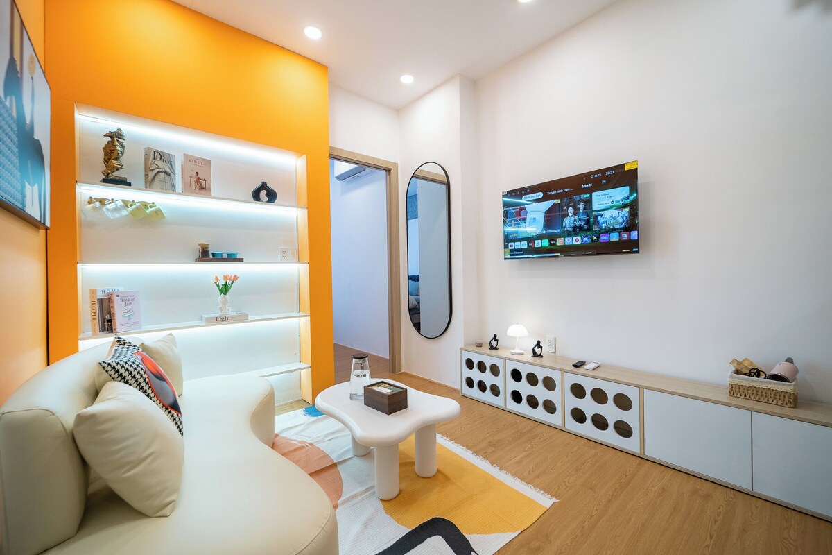 A modern living room with a sofa, a coffee table, a TV mounted on the wall, and a bookshelf.