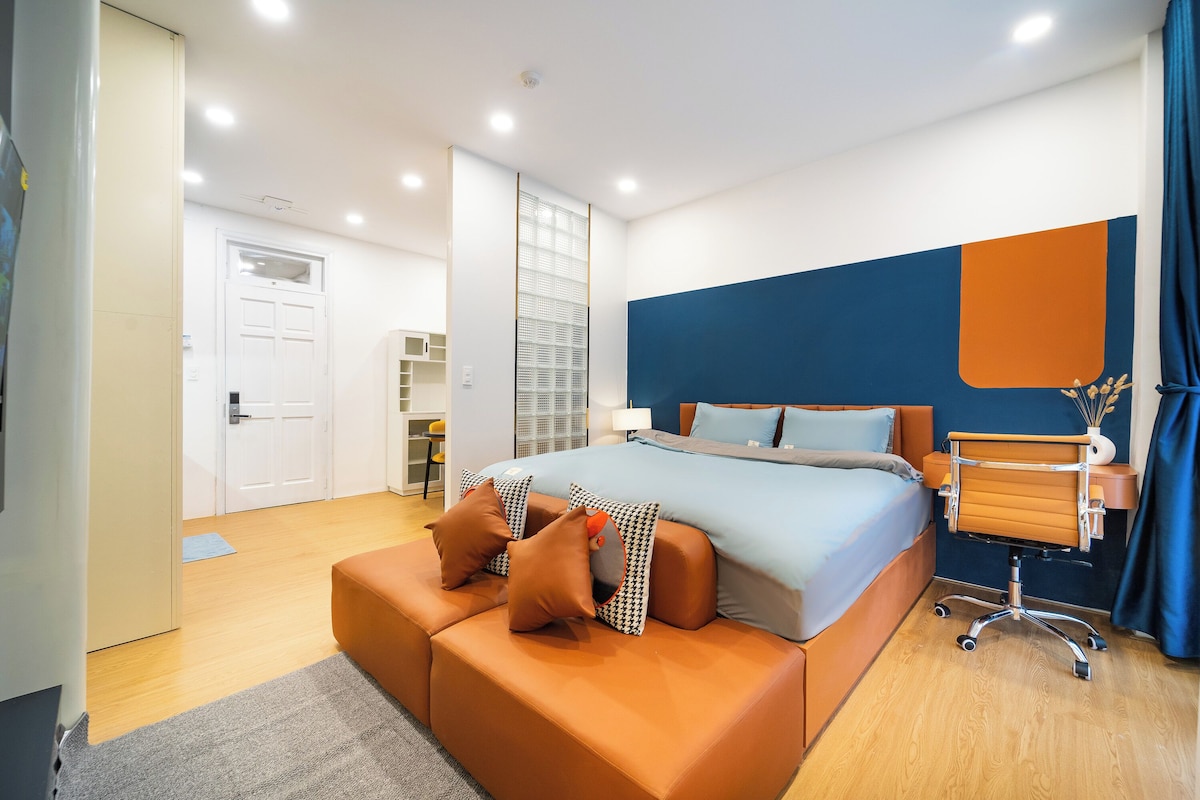 A modern bedroom with a bed, a seating area, and a desk.
