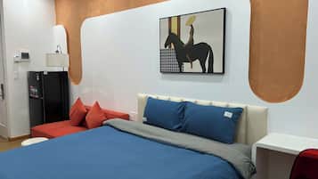 Quarto de hotel com cama, escrivaninha, frigorífico e uma obra de arte na parede.